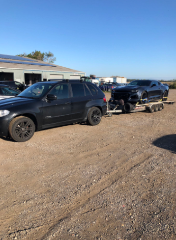 Black SUV towing a sports car on a trailer at a transport facility