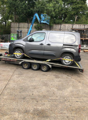 Grey utility van secured on a transport trailer