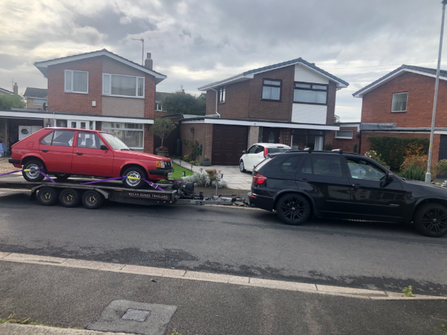 Red vintage car on a trailer outside a residential collection address